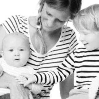 A woman holds a baby while a young child, smiling and gently touching the baby's hand, enjoys the moment. All three in striped shirts create a bright scene—perfect inspiration for gifts for one year old or baby toys 12-18 months.