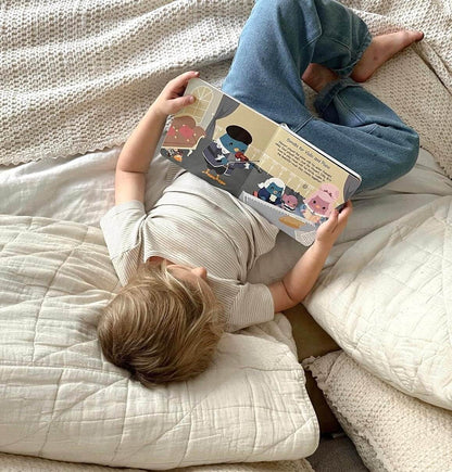 A young child lies on a white bed, reading Ditty Bird UK's "Music of Mozart"—a perfect educational book and first birthday gift that introduces little ones to classical music.