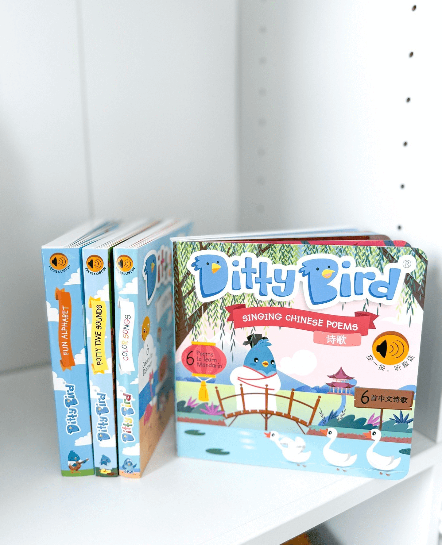 Four vibrant Ditty Bird UK children's books sit on a white shelf, with "Chinese Children's Songs in Mandarin Vol.2" facing forward—showcasing birds, ducks, and a garden scene—perfect for early learning or as a first birthday gift.