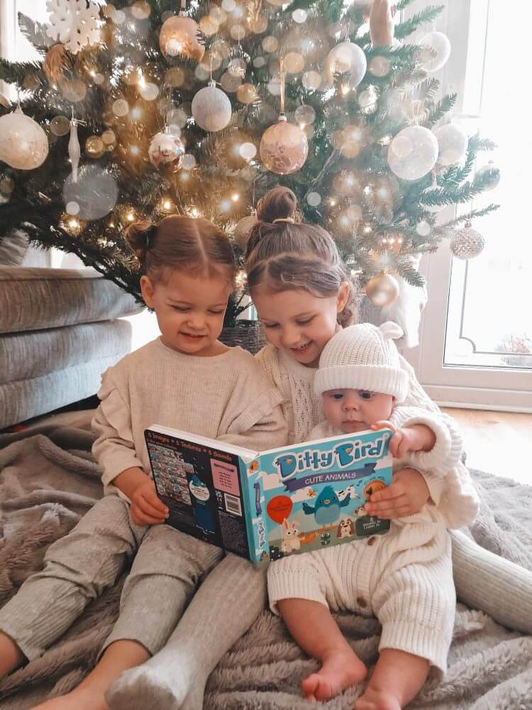 Three young children sit on a rug by a decorated Christmas tree, reading Ditty Bird UK's "Cute Animals Touch, Feel & Listen" book—an ideal first birthday gift or baby toy for ages 6-12 months.