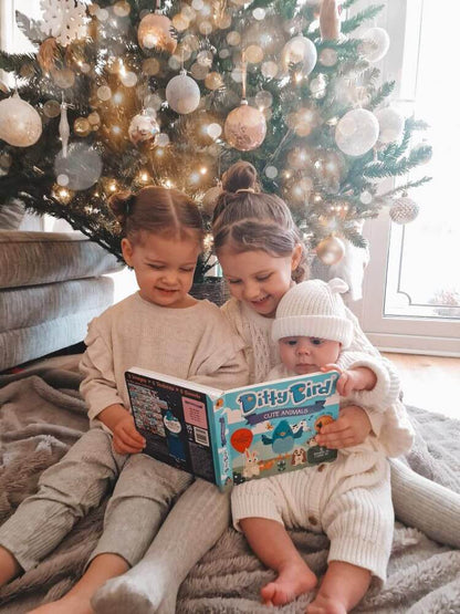 Three young children sit on a rug by a decorated Christmas tree, reading Ditty Bird UK's "Cute Animals Touch, Feel & Listen" book—an ideal first birthday gift or baby toy for ages 6-12 months.